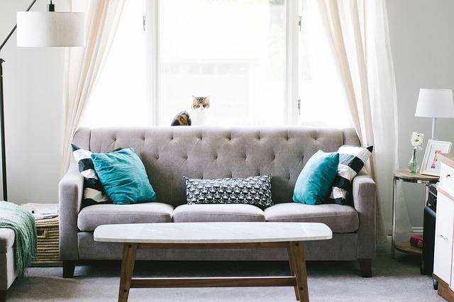 grey tufted couch with throw pillows and coffee table in front of a window